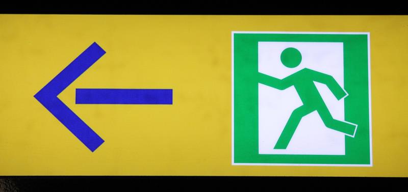 An emergency exit sign with a green figure running next to a blue arrow on yellow background. 