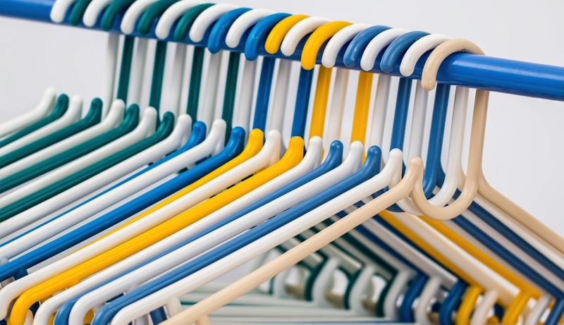 Close-up of a row of colorful plastic hangers on a blue rod, including blue, yellow, beige and green. The image conveys a sense of organisation and brightness.